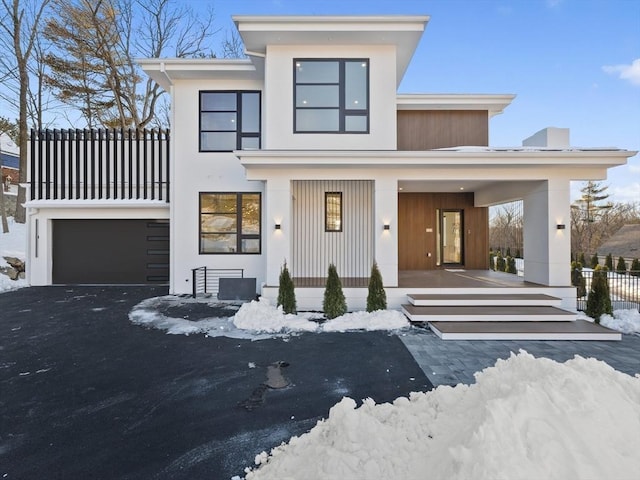 view of front of house featuring an attached garage, covered porch, aphalt driveway, and stucco siding