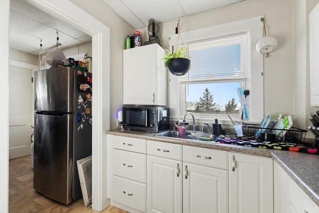 kitchen with a paneled ceiling, white cabinetry, sink, stainless steel fridge, and light wood-type flooring