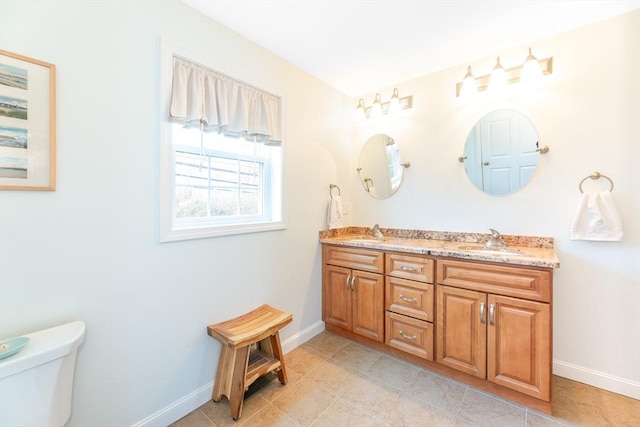 bathroom featuring a sink, baseboards, toilet, and double vanity