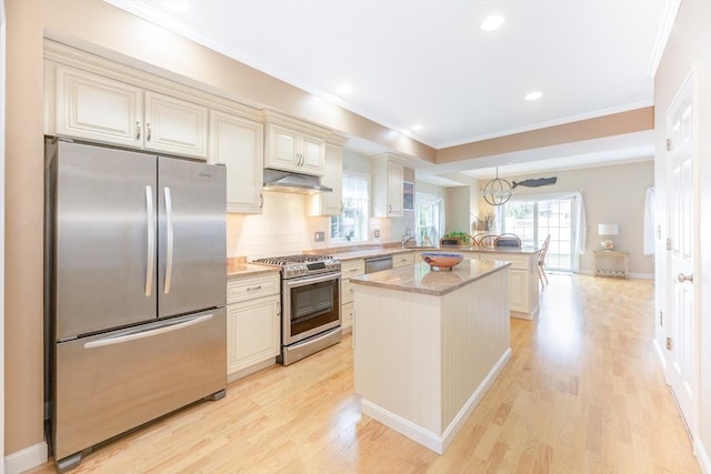 kitchen featuring cream cabinets, crown molding, appliances with stainless steel finishes, light wood-style floors, and a peninsula