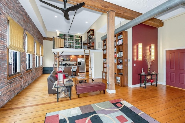 living area with a towering ceiling, brick wall, baseboards, ceiling fan, and light wood-style flooring