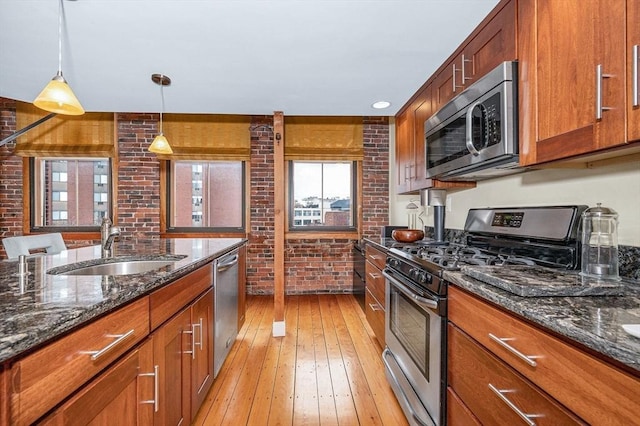 kitchen featuring brick wall, brown cabinets, a sink, light wood finished floors, and stainless steel appliances
