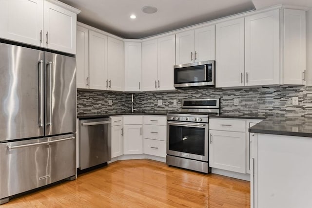 20 Winfield St Unit 1, Boston, MA 02127 - kitchen featuring stainless steel appliances, dark countertops, light wood-style floors, white cabinetry, and decorative backsplash