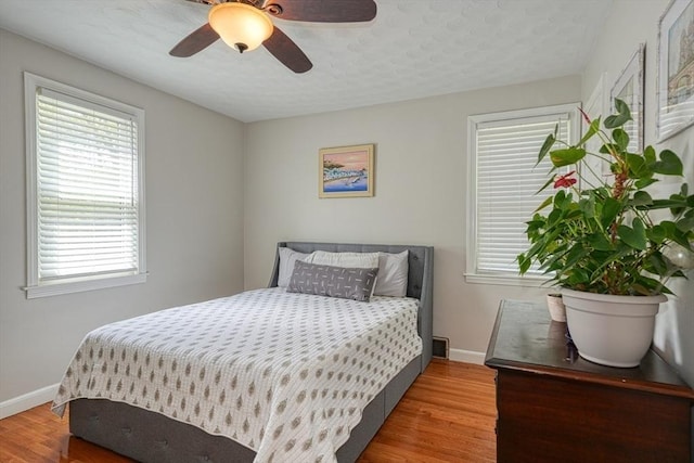 bedroom featuring wood finished floors, multiple windows, baseboards, and a ceiling fan