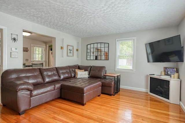 living area with light wood-style flooring, plenty of natural light, baseboards, and a textured ceiling
