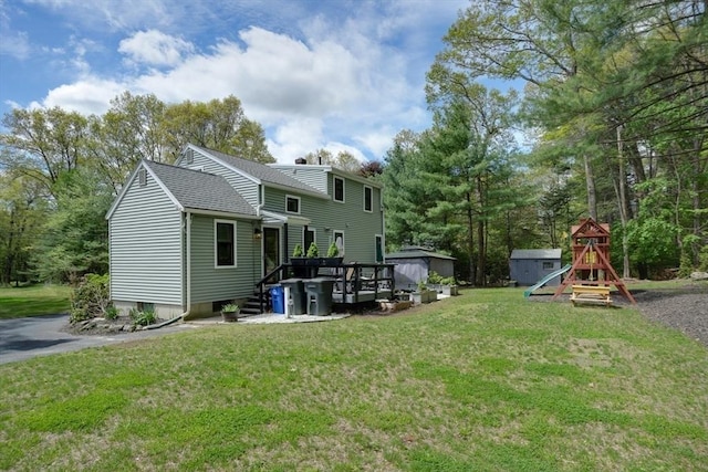 rear view of property with a storage shed, a playground, an outdoor structure, a shingled roof, and a yard