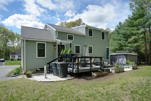 rear view of property with a lawn, roof with shingles, a storage unit, and an outbuilding