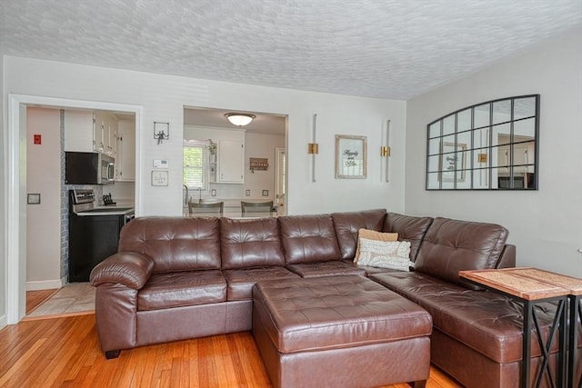 living area with a textured ceiling, light wood-type flooring, and baseboards
