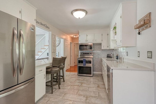 kitchen with stainless steel appliances, a sink, light countertops, and white cabinetry