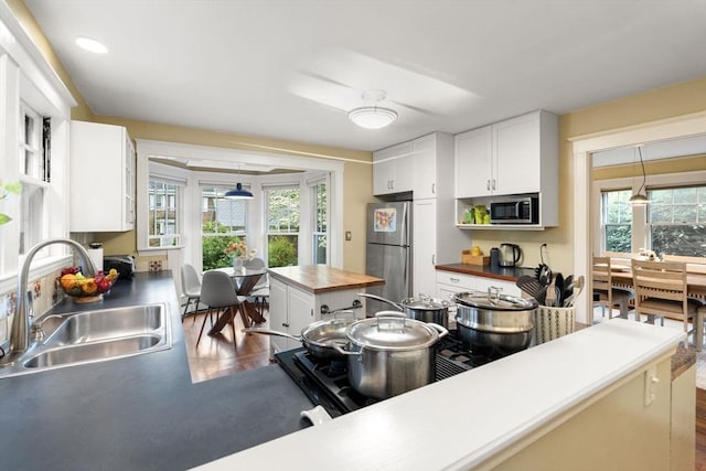kitchen with a sink, stainless steel appliances, white cabinetry, hanging light fixtures, and butcher block countertops