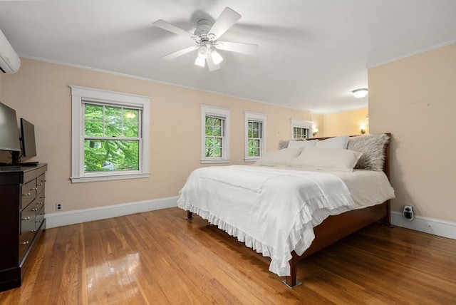 bedroom with baseboards, hardwood / wood-style floors, ornamental molding, ceiling fan, and a wall mounted AC