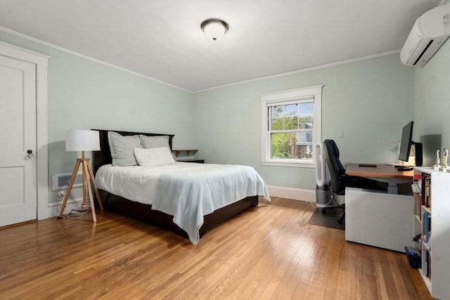 bedroom with a wall mounted air conditioner, light wood-style floors, crown molding, baseboards, and a desk