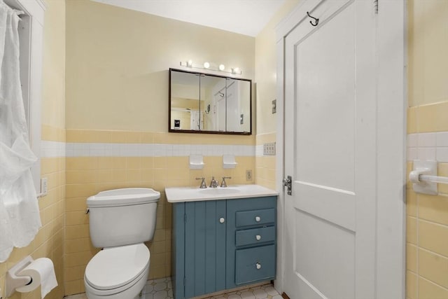 bathroom featuring tile walls, wainscoting, toilet, and vanity