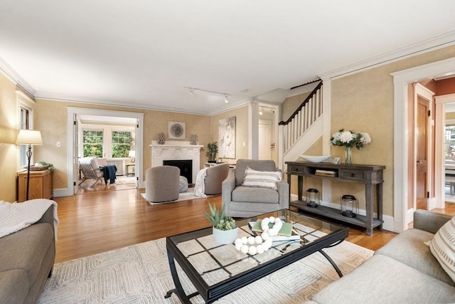 living room with stairs, light wood-style floors, rail lighting, crown molding, and baseboards