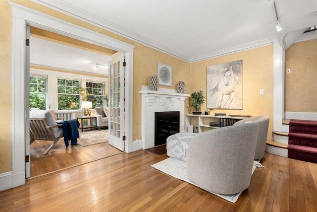 living area with hardwood / wood-style flooring, rail lighting, ornamental molding, a brick fireplace, and baseboards