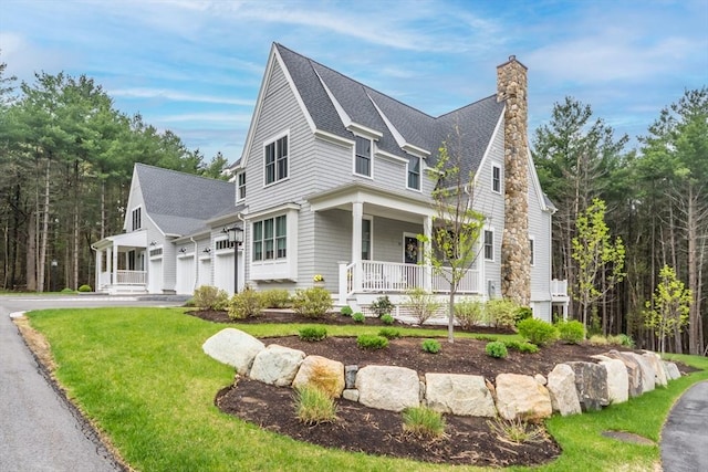 view of front of home featuring covered porch, aphalt driveway, a chimney, a front lawn, and a shingled roof