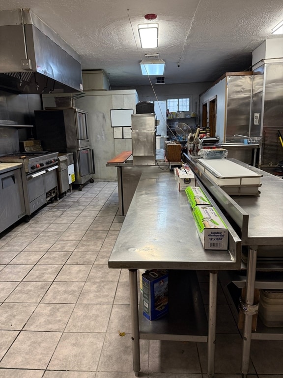 kitchen featuring a textured ceiling, range hood, high end stainless steel range, gray cabinets, and light tile patterned flooring