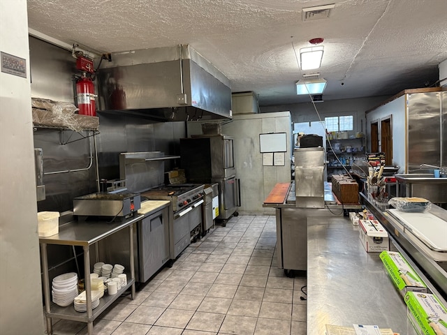 kitchen featuring light tile patterned flooring, stainless steel stove, a textured ceiling, and exhaust hood