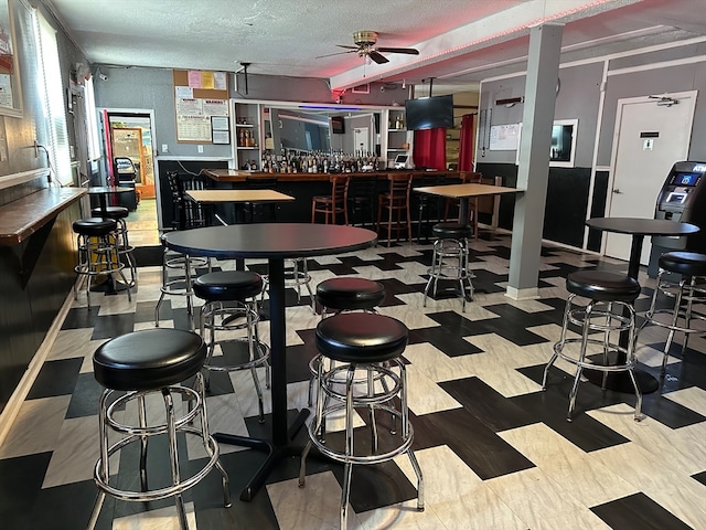 dining area featuring a textured ceiling, indoor bar, and ceiling fan