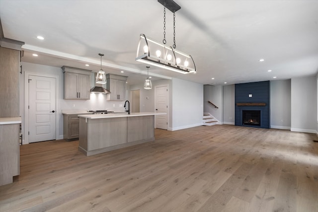 kitchen featuring a large fireplace, pendant lighting, gray cabinets, light hardwood / wood-style floors, and an island with sink