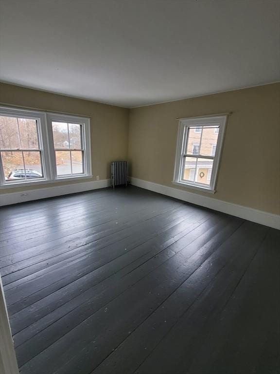 empty room featuring dark wood-type flooring, radiator heating unit, and a wealth of natural light