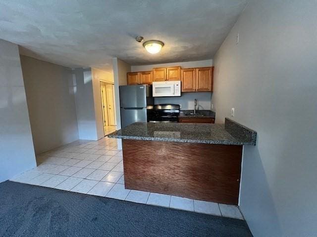 kitchen with refrigerator, sink, dark stone counters, stove, and light carpet