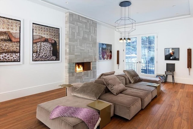 living room with baseboards, a tiled fireplace, ornamental molding, wood finished floors, and an inviting chandelier