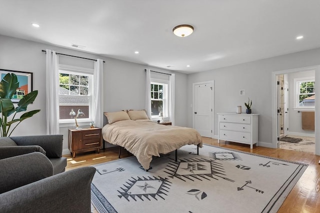 bedroom with connected bathroom, light hardwood / wood-style floors, and multiple windows