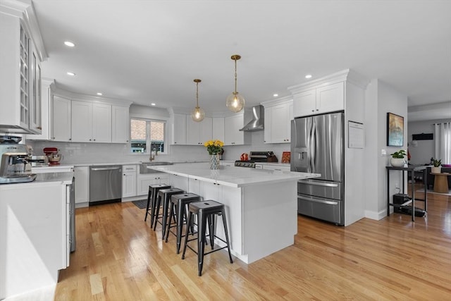 kitchen with wall chimney range hood, a kitchen island, white cabinets, decorative light fixtures, and stainless steel appliances