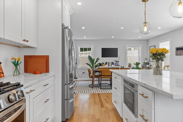 kitchen featuring light stone countertops, pendant lighting, white cabinets, stainless steel appliances, and light hardwood / wood-style floors