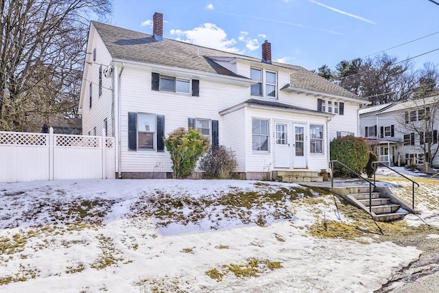 view of front of house featuring entry steps, roof with shingles, fence, and a chimney