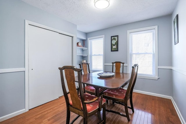 dining space featuring built in features, baseboards, a textured ceiling, and hardwood / wood-style floors