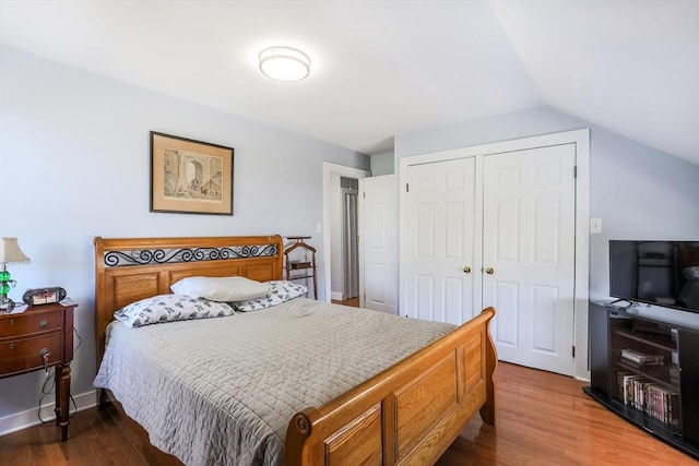 bedroom with lofted ceiling, a closet, wood finished floors, and baseboards