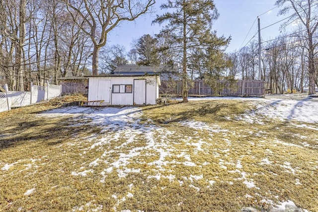 snow covered structure with an outbuilding, fence, and a storage shed