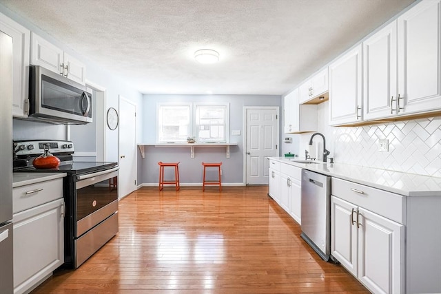 kitchen with tasteful backsplash, appliances with stainless steel finishes, light countertops, light wood-type flooring, and a sink