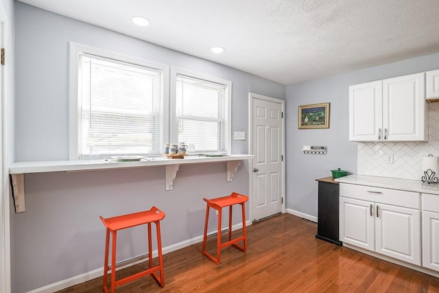 kitchen featuring dark wood finished floors, a kitchen bar, backsplash, white cabinetry, and baseboards