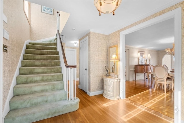 stairs featuring a notable chandelier, wallpapered walls, crown molding, and wood finished floors