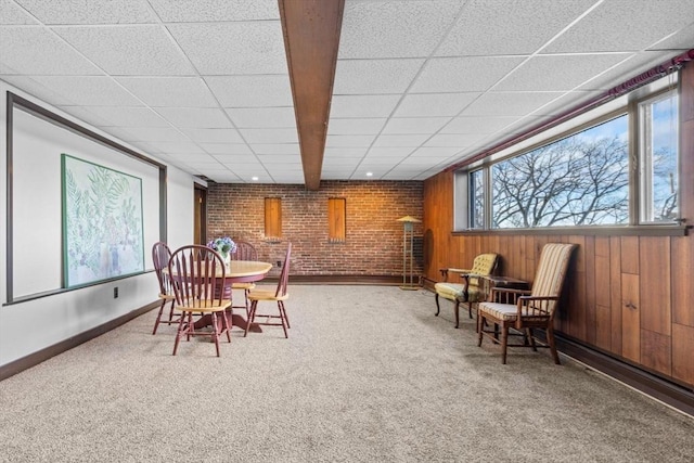 carpeted dining area with brick wall, a paneled ceiling, baseboards, and wood walls