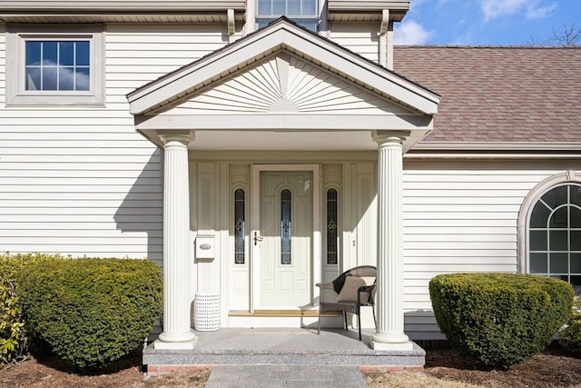 doorway to property with covered porch and a shingled roof