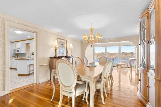 dining area with a chandelier, arched walkways, crown molding, and light wood-style floors