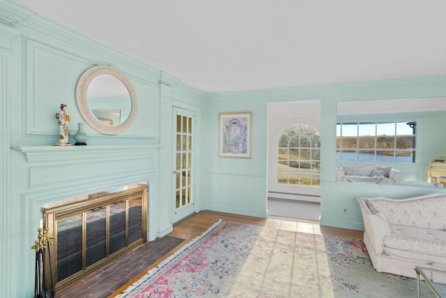 living area featuring crown molding, a fireplace with flush hearth, wood finished floors, and a baseboard radiator