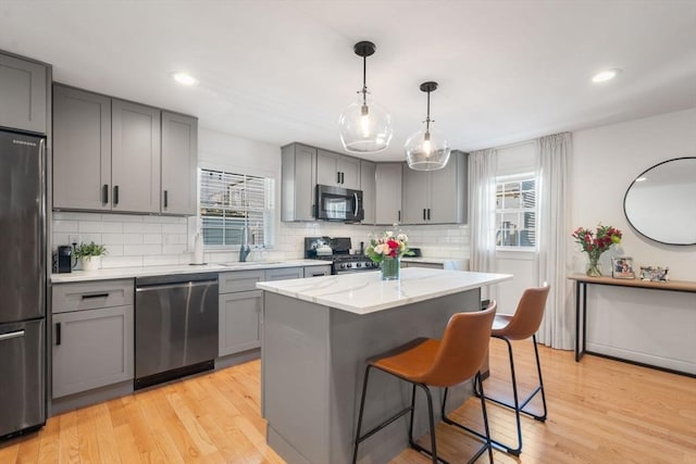 kitchen with light wood finished floors, appliances with stainless steel finishes, gray cabinets, and a center island