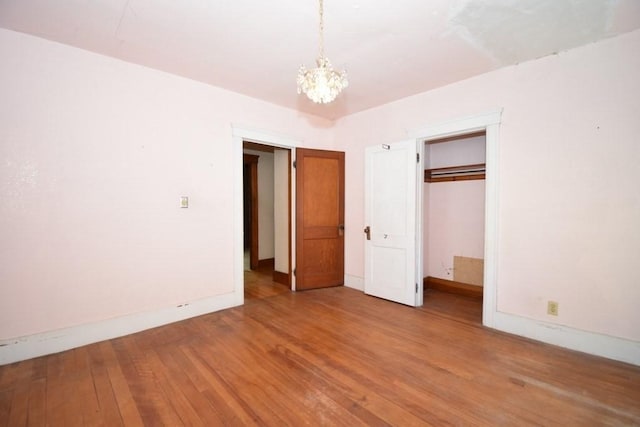 unfurnished bedroom with an inviting chandelier, baseboards, a closet, and wood finished floors