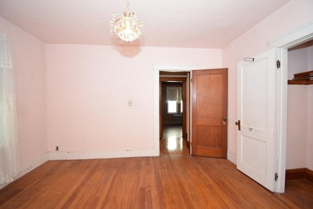 empty room with baseboards, wood finished floors, and a notable chandelier