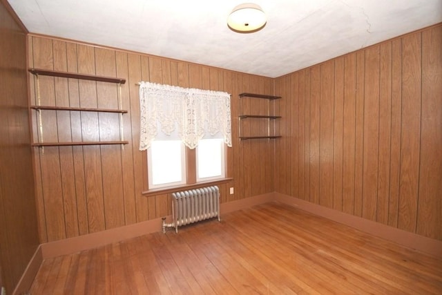 unfurnished room with hardwood / wood-style flooring, wood walls, baseboards, and radiator