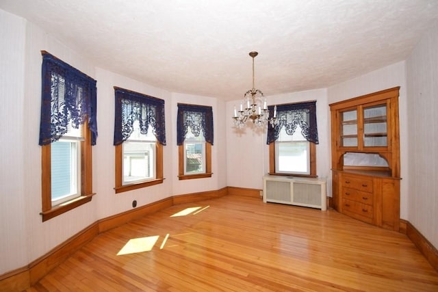 unfurnished dining area featuring light wood-style floors, radiator, an inviting chandelier, and a healthy amount of sunlight