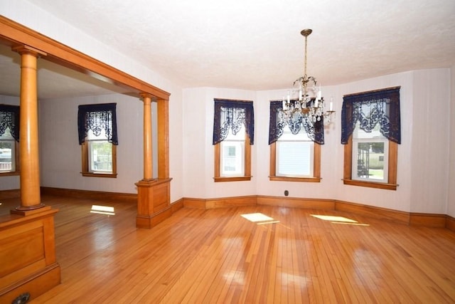 unfurnished dining area featuring a notable chandelier, decorative columns, baseboards, and hardwood / wood-style flooring