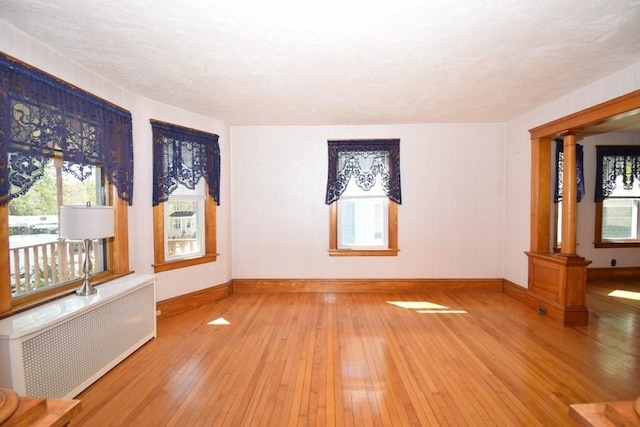 unfurnished room with radiator heating unit, baseboards, decorative columns, and hardwood / wood-style flooring