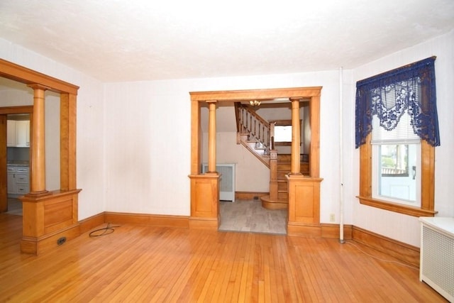 unfurnished living room featuring stairs, radiator, decorative columns, baseboards, and light wood-type flooring