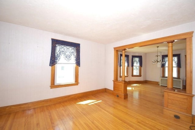 unfurnished room featuring ornate columns, radiator, a notable chandelier, and hardwood / wood-style flooring
